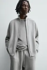 Chaqueta de punto compacto con mezcla de algodón, corte relajado, cuello subido, manga larga, bolsillos laterales de vivo y cierre frontal con cremallera.