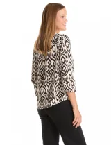Blusa de seda fría con estampado geométrico tipo ikat en tonos beige y negro. Presenta escote en V, botones decorativos en la parte frontal y mangas tres cuartos con detalle de tajo en los puños.