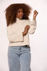 Buzo tejido de punto color beige, con cuello alto, mangas largas con puños anchos acanalados y ruedo también acanalado. Presenta un diseño de hombros caídos y corte holgado.