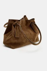 Bolso tipo shopper de piel en color marrón, con doble asa de hombro, bolsillo interior con cremallera y doble sistema de cierre con botón imantado y tira con botón metálico.