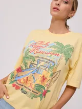 Remera amarilla de algodón con estampado de playa hawaiana con palmeras, flores y tabla de surf.