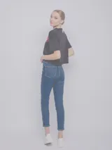 Pantalón de jean chupín gris oscuro con cuatro bolsillos, botón y cierre metálicos.