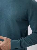 Sweater de tejido de punto fino en color gris, con cuello redondo, mangas largas y puños acanalados. Presenta un diseño liso con un pequeño detalle bordado en el pecho.
