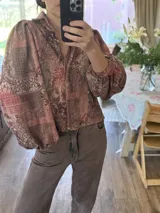 Camisa de corte holgado con estampado estilo patchwork en tonos tierra, cuello clásico, cierre frontal con botones y mangas largas abullonadas con puños elásticos.