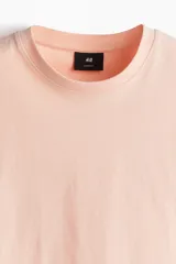 Remera color salmón de corte holgado, cuello redondo y mangas cortas.