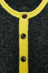 Chaqueta de punto con diseño color block, cuello redondo y manga larga. Presenta cuerpo en color gris oscuro, mangas en gris claro y detalles de ribetes en color amarillo vibrante. Cierre frontal con botones oscuros.