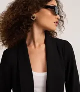 Blazer negro confeccionado en tejido airflow, con solapa en el cuello y abertura total. La prenda tiene martingalas en los puños, que son tiras con botones.
