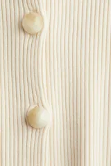 Saco ajustado en punto acanalado color beige, con cuello redondo, cierre frontal con botones jaspeados, hombros caídos y mangas largas con puños ceñidos.