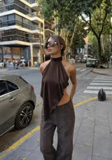 Top de satén color marrón con escote halter y diseño asimétrico en punta. Posee espalda descubierta y cierre con lazo fino en el cuello.