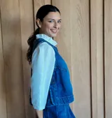 Chaleco de corte recto y largo a la cintura, confeccionado en denim con estampado de rayas verticales en tonos azul y blanco. Presenta cuello redondo y costuras visibles que definen su estructura.