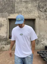 Remera blanca de algodón con corte boxy y parche bordado con la palabra "Brokers" en óvalo azul y verde.