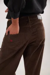 Pantalón de pana de corte ancho y tiro medio-bajo, con diseño de cinco bolsillos y acabado lavado. Presenta un aplique cuadrado decorativo en una de las piernas y un pin bordado de la marca.
