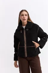 Campera tipo teddy de textura suave y acabado de peluche en color beige. Presenta cuello amplio con detalle de hebilla, cierre frontal y recortes en contraste de color marrón que marcan la estructura de la prenda.