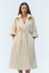 Trench coat oversize color beige, largo, con doble botonadura, solapas amplias, bolsillos laterales y cinturón ajustable para anudar.