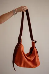 Bolso tipo hobo de gamuza color naranja quemado, con correa ancha de tela color bordó.