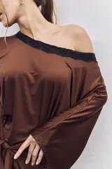 Vestido corto de satén color marrón, con diseño de un solo hombro y detalle de encaje negro en el escote y el ruedo. Presenta un nudo frontal con caída de tela y mangas largas.