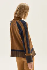 Polera de cuello alto confeccionada en lana lambswool, con diseño de bloques de color en tonos beige y marrón. Presenta mangas raglán con textura acanalada y detalles en hilo metalizado lurex.