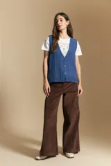 Chaleco tejido color azul, con escote en V, cierre frontal con botones y diseño de líneas verticales en relieve. Presenta terminaciones acanaladas en el ruedo y un borde ondulado en el escote.