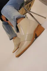 Botín de cuero color crema con puntera cuadrada, elástico lateral plateado y detalle de tira con textura reptil cruzada sobre el empeine.