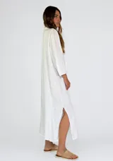 Vestido largo color beige de lino, con cuello mao, mangas 3/4 abullonadas y cierre frontal con botones. Presenta volantes verticales en el frente.