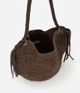 Bolso de playa tipo canasta, tejido en fibra de papel color marrón oscuro, con forma redondeada y abertura superior curva. Cuenta con asas trenzadas de material sintético marrón oscuro y detalles de flecos colgantes a los lados.