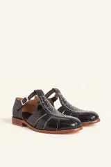 Sandalias de cuero color marrón, tipo romanas, con talón cerrado, tira en T con detalles de tachas metálicas, aberturas laterales y cierre de hebilla ajustable. Tienen tacón bajo de madera.