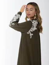 Maxi vestido camisero de lino blanco con bordados en tono beige en mangas y ruedo. Presenta cuello camisero, botones frontales y mangas largas.