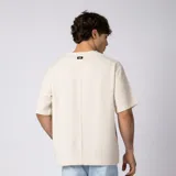 Remera oversize de lino entramado color blanco off-white, con cuello redondo, mangas cortas de hombro caído y etiqueta aplicada en el borde inferior.