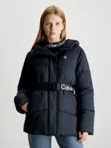 Campera puffer negra de nailon con capucha y cinturón con hebilla. Tiene cierre de cremallera y botón de presión, bolsillos en la cintura y logo monograma de Calvin Klein estampado en el pecho.