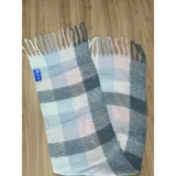 Bufanda rectangular de tejido grueso con diseño de cuadros en tonos pastel, gris y blanco, terminada con flecos en los extremos.