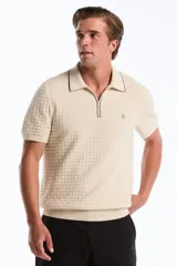 Chomba de punto color beige, de manga corta, con cuello polo, cierre frontal parcial y textura en relieve. Presenta ribetes oscuros en el cuello y el logotipo bordado del pingüino en el pecho.