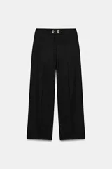 Pantalón negro de tiro medio con pierna ancha y cierre frontal de cremallera con dos botones dorados decorativos.