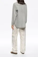 Pantalón de corte barrel color negro, con tiro medio, cierre frontal con botón y cremallera, cinco bolsillos y detalle de tachas metálicas a lo largo de las costuras laterales.