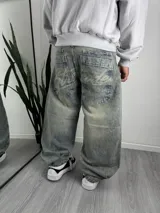 Jeans baggy de mezclilla color celeste con efecto desgastado, tiro medio y corte ancho en las piernas. Presenta bolsillos traseros grandes con costuras detalladas y estampado tipográfico.