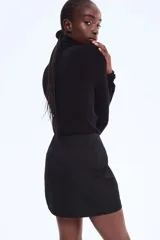 Pollera corta negra de tiro alto, con cierre oculto y pinzas en la espalda.