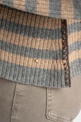 Sweater de tejido de punto con diseño de rayas horizontales alternando gris y beige. Presenta cuello redondo y mangas largas con costura decorativa visible en los laterales.