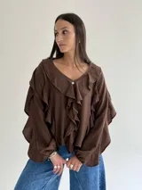 Blusa color marrón chocolate con escote en V, decorada con volados frontales y en las mangas. Presenta mangas largas con puños elásticos y un corte holgado.