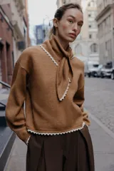 Jersey de punto color marrón, manga larga y corte holgado, con cuello tipo bandana anudado y terminaciones con puntilla blanca a contraste.