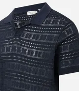 Remera tipo polo de manga corta con cuello en V, confeccionada en un tejido con textura patchwork. Presenta un diseño elegante y versátil, ideal para un look casual o formal.