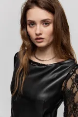 Vestido corto de símil cuero negro, de corte recto, escote amplio y sin mangas, combinado con mangas largas de encaje negro.