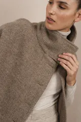 Capa color beige con textura de espiga, cuello alto con botones y aberturas laterales para los brazos. Confeccionada en lana fina sin teñir.