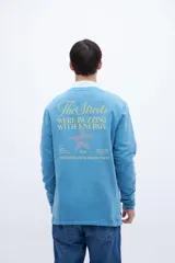 Buzo gris de felpa liviana con cuello redondo, mangas largas y puños ajustados. Tiene un bordado pequeño en el pecho y un diseño estampado en la espalda.