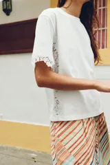 Camiseta blanca de manga corta y cuello redondo, confeccionada en hilatura de algodón con detalle de aplicación de encaje a tono en las mangas y los laterales.
