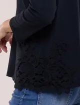 Remera negra de silueta recta y escote redondo, confeccionada en algodón y elastano. Presenta mangas tres cuartos y apliques de guipure calado en los laterales del ruedo.