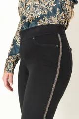 Pantalón de jean negro alicrado, modelo calza sin cierre, con faja en la cintura y aplique de galón bordado en los costados.