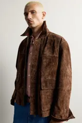 Parka de piel marrón tipo gamuza con cuello solapa, manga larga con puños de botones a presión y múltiples bolsillos de plastrón con solapa en el pecho y la cadera. Cierre frontal de cremallera oculta con solapa.