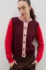 Saco de punto con diseño color block, presenta cuerpo en color bordó, mangas en color rojo y tapeta frontal con cuello redondo en color rosado. Posee cierre frontal con botones y puños acanalados.