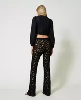 Pantalón acampanado negro confeccionado en algodón tejido a crochet con estampado floral, bordes festoneados, cintura elástica y forro corto en contraste.