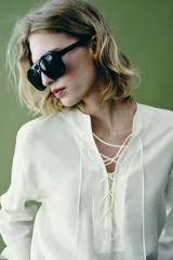 Camisa blanca ZARA Woman Collection de 100% seda, con escote en V ajustable con cordones entrelazados y manga larga con puños rectos.