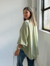 Camisa verde claro de corte oversize, con mangas tres cuartos abullonadas, escote en V con cuello camisero y cierre frontal parcial de botones. Cuenta con delicados bordados florales tono sobre tono distribuidos por toda la prenda.